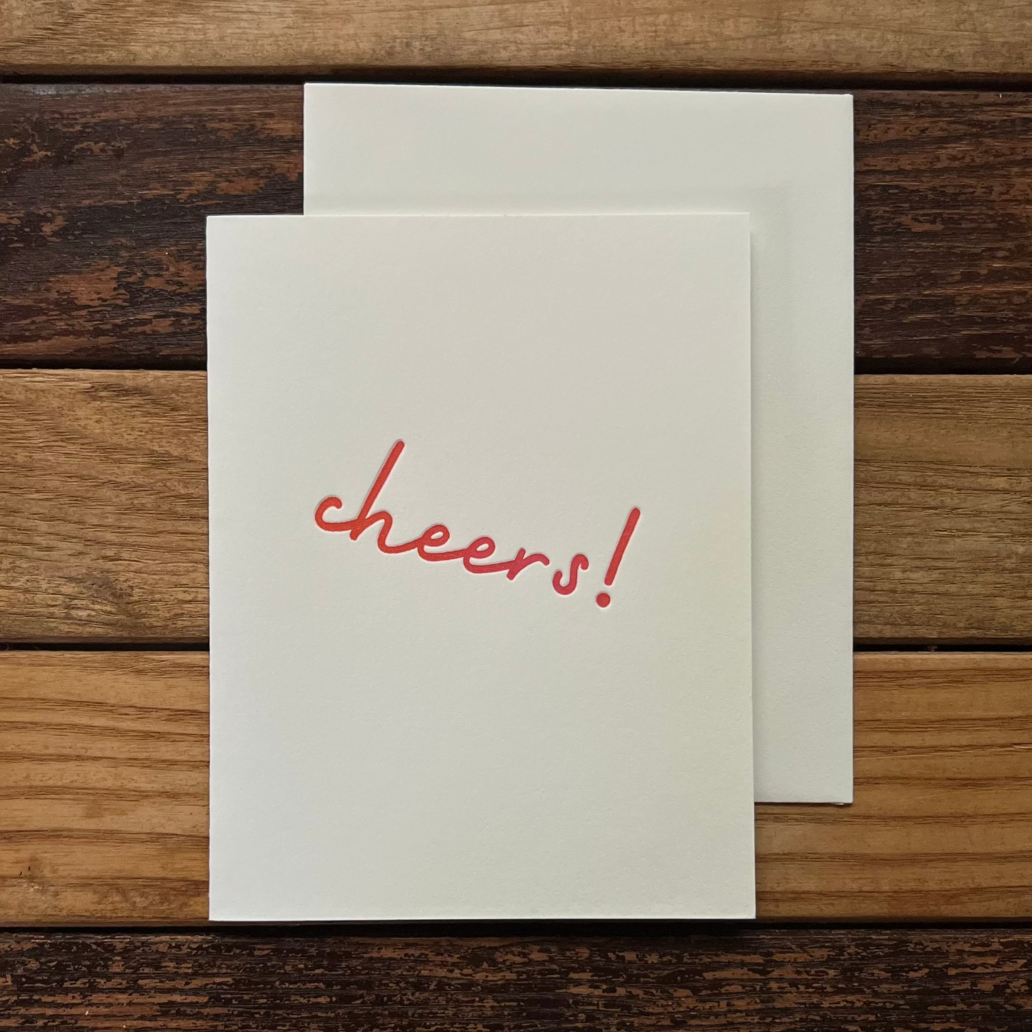 White card with 'cheers!' in orange on a wooden surface