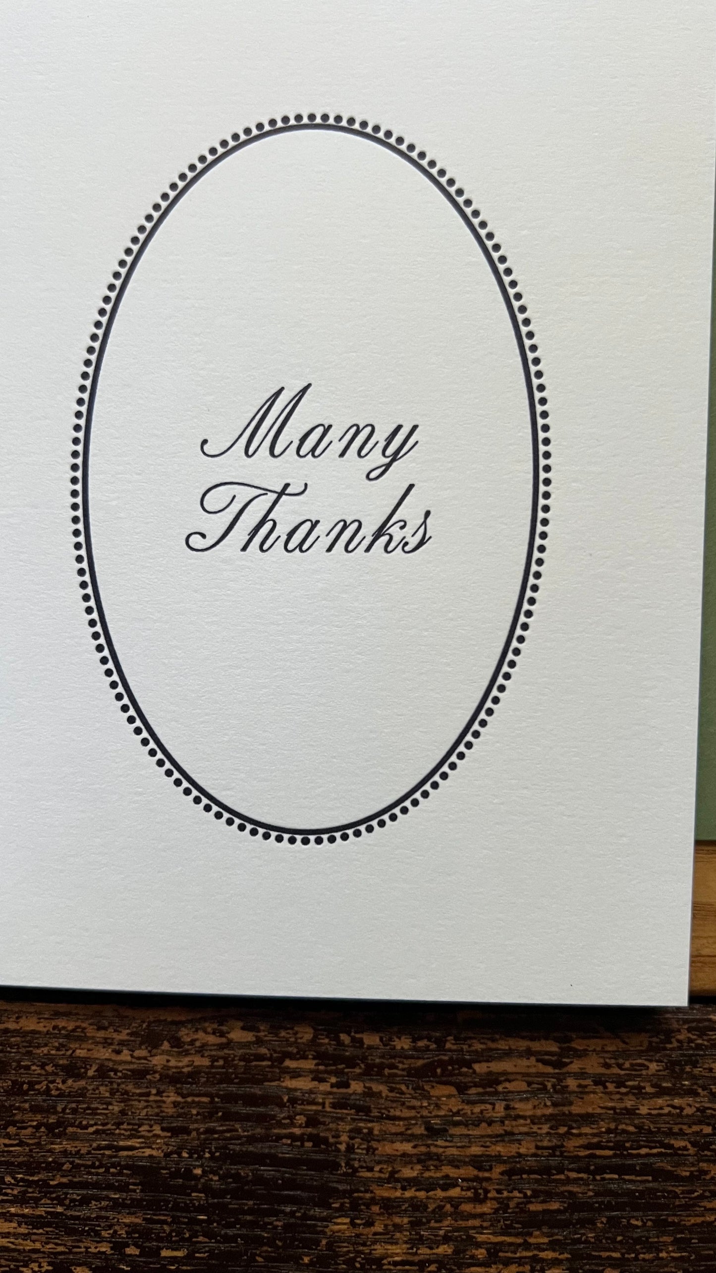 White card with 'Many Thanks' text in an oval frame on a wooden surface