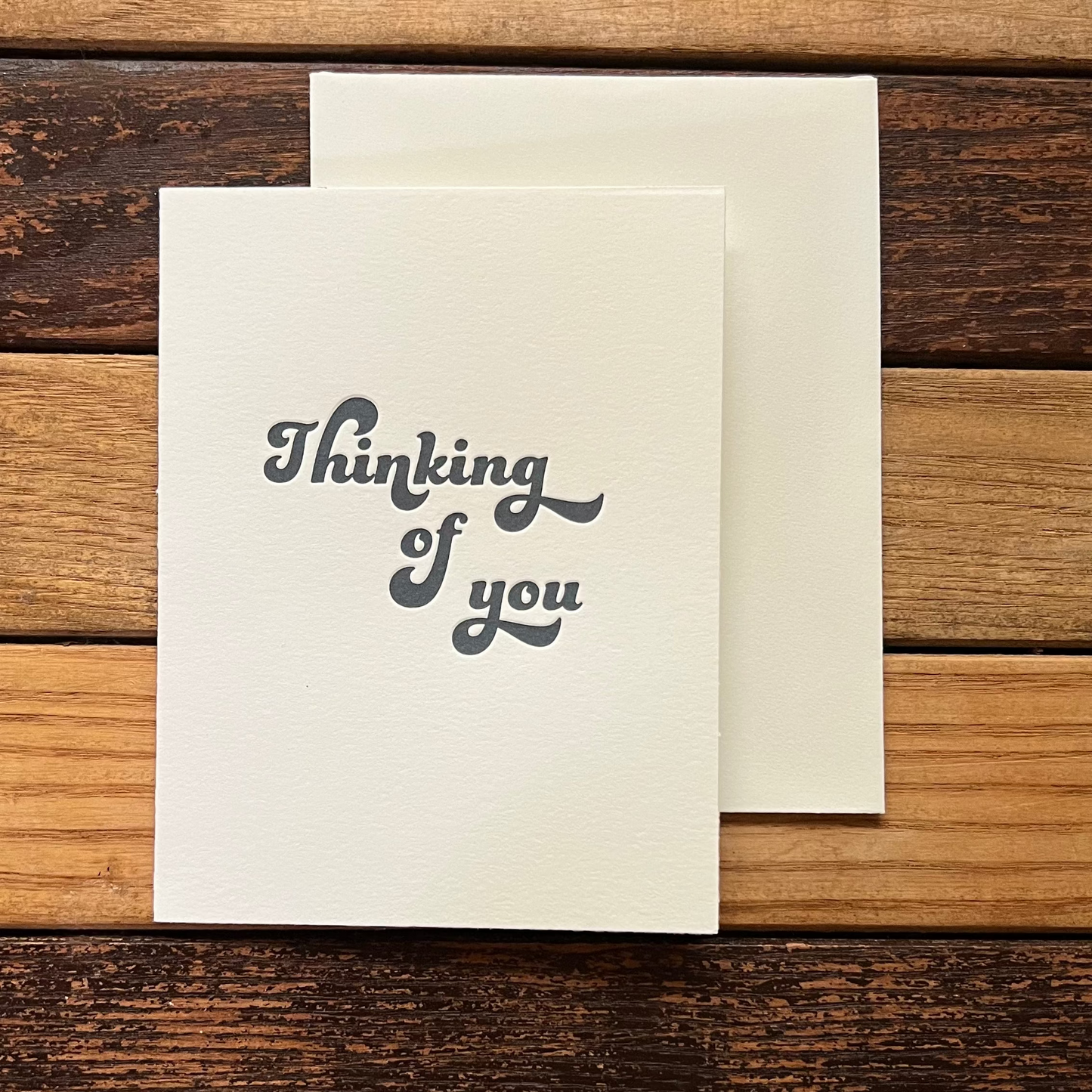 Note card with 'Thinking of you' text on a wooden surface