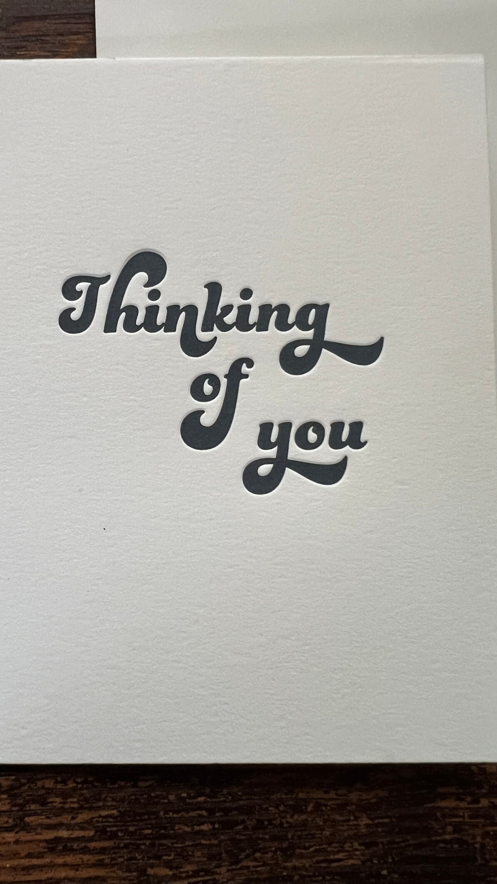 White card with 'Thinking of you' text on a wooden surface
