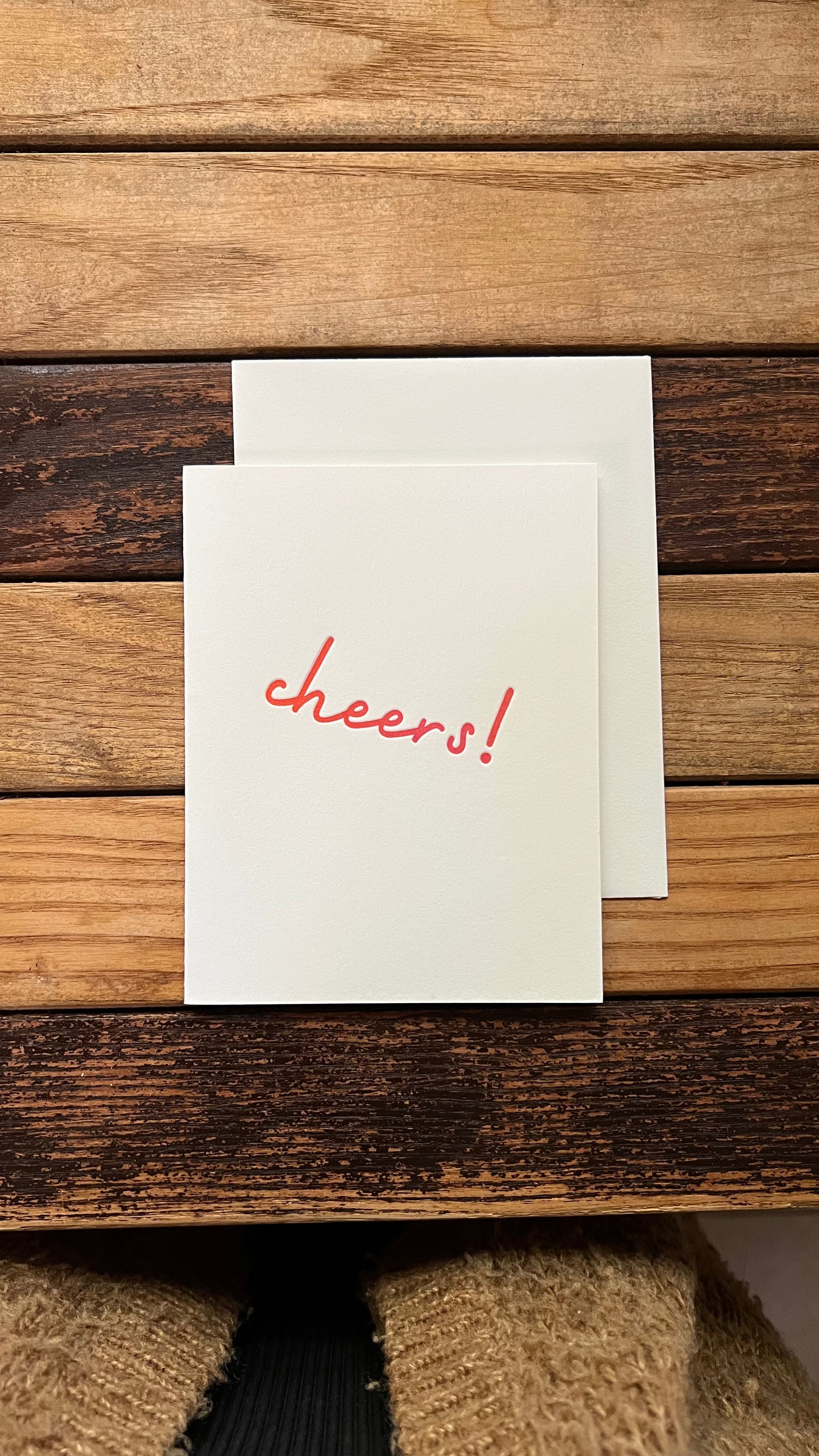 card on a wooden surface, one with 'cheers!' printed on it.