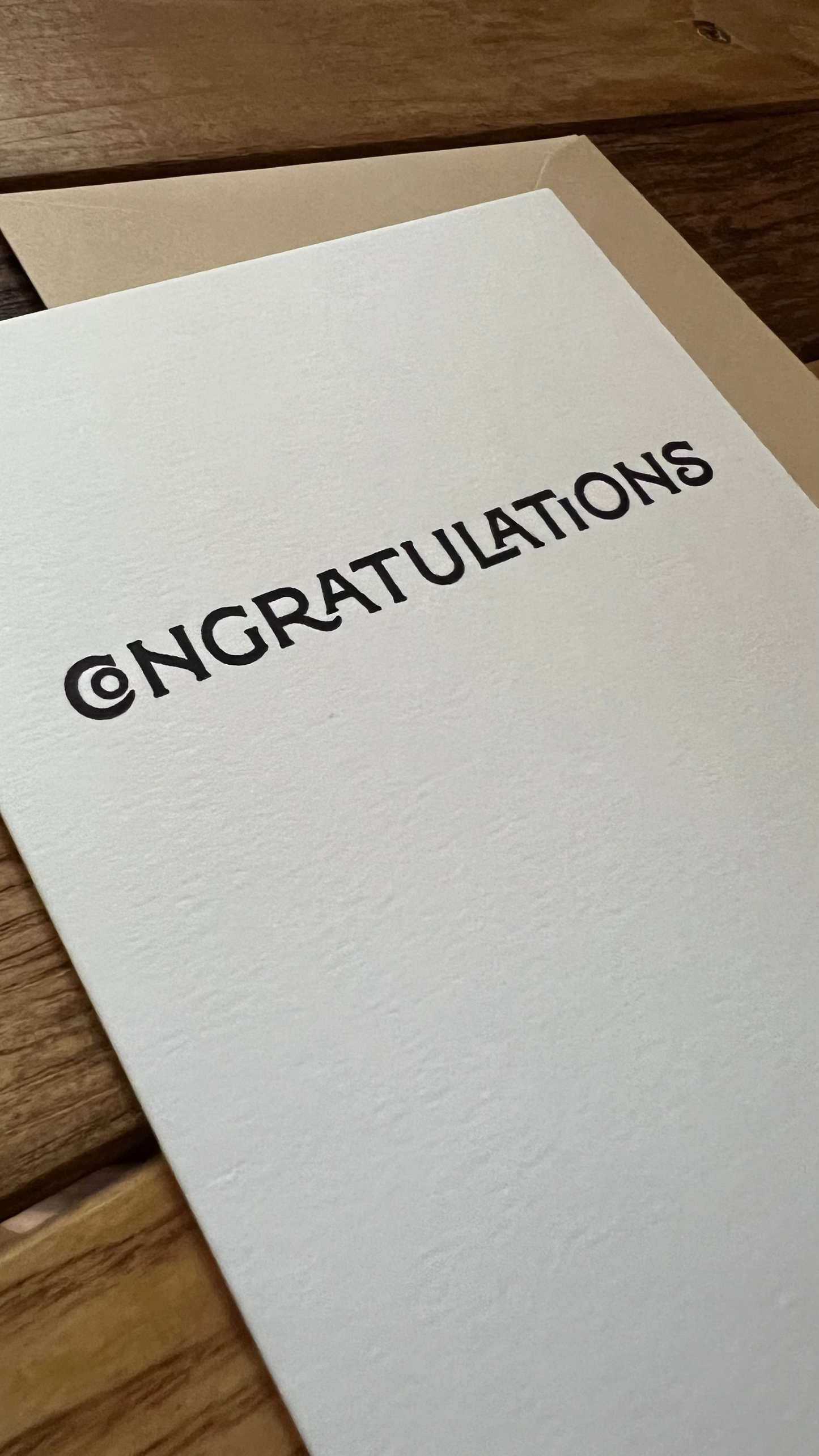White card with 'CONGRATULATIONS' printed on it, lying on a wooden surface.