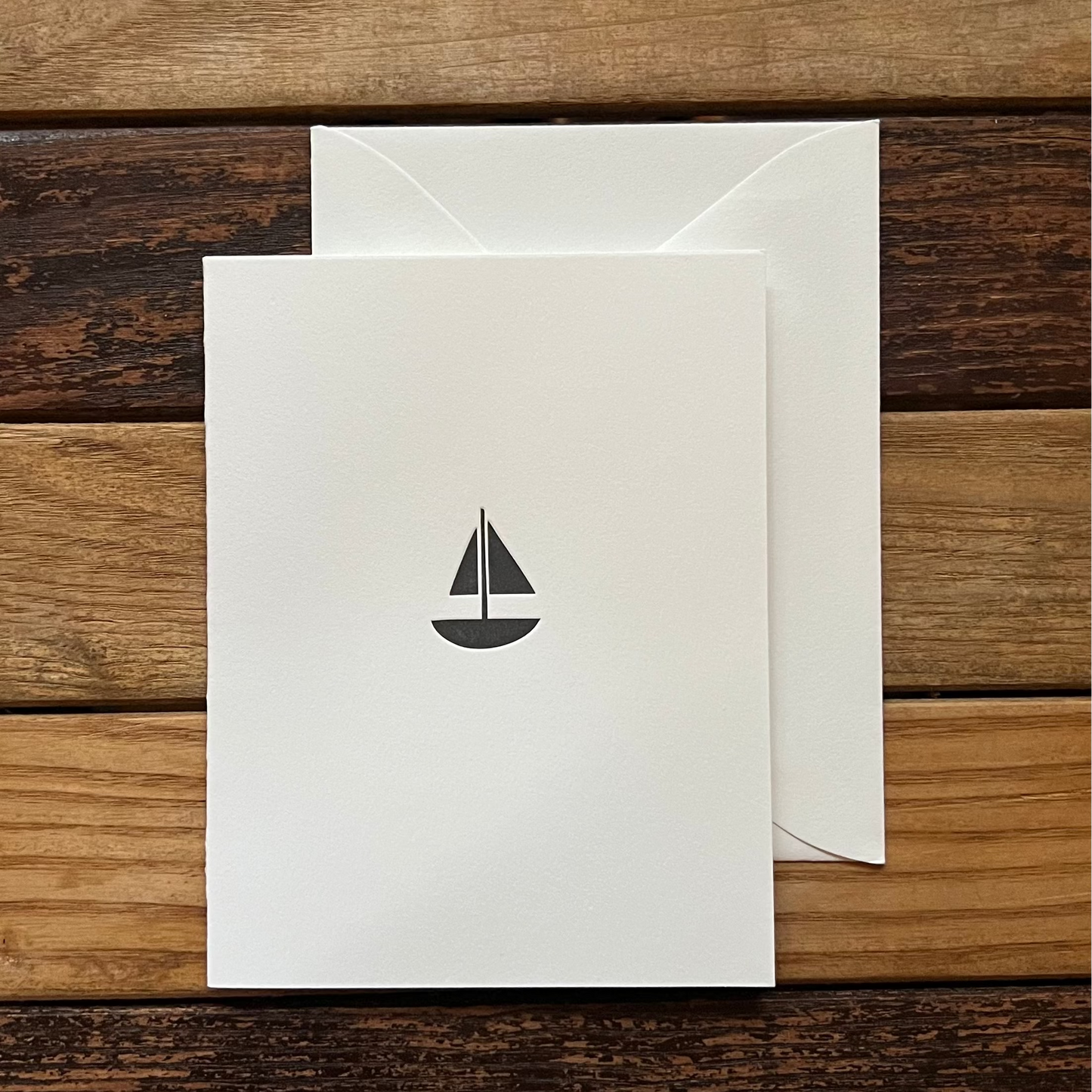 White card with a black sailboat design on a wooden surface