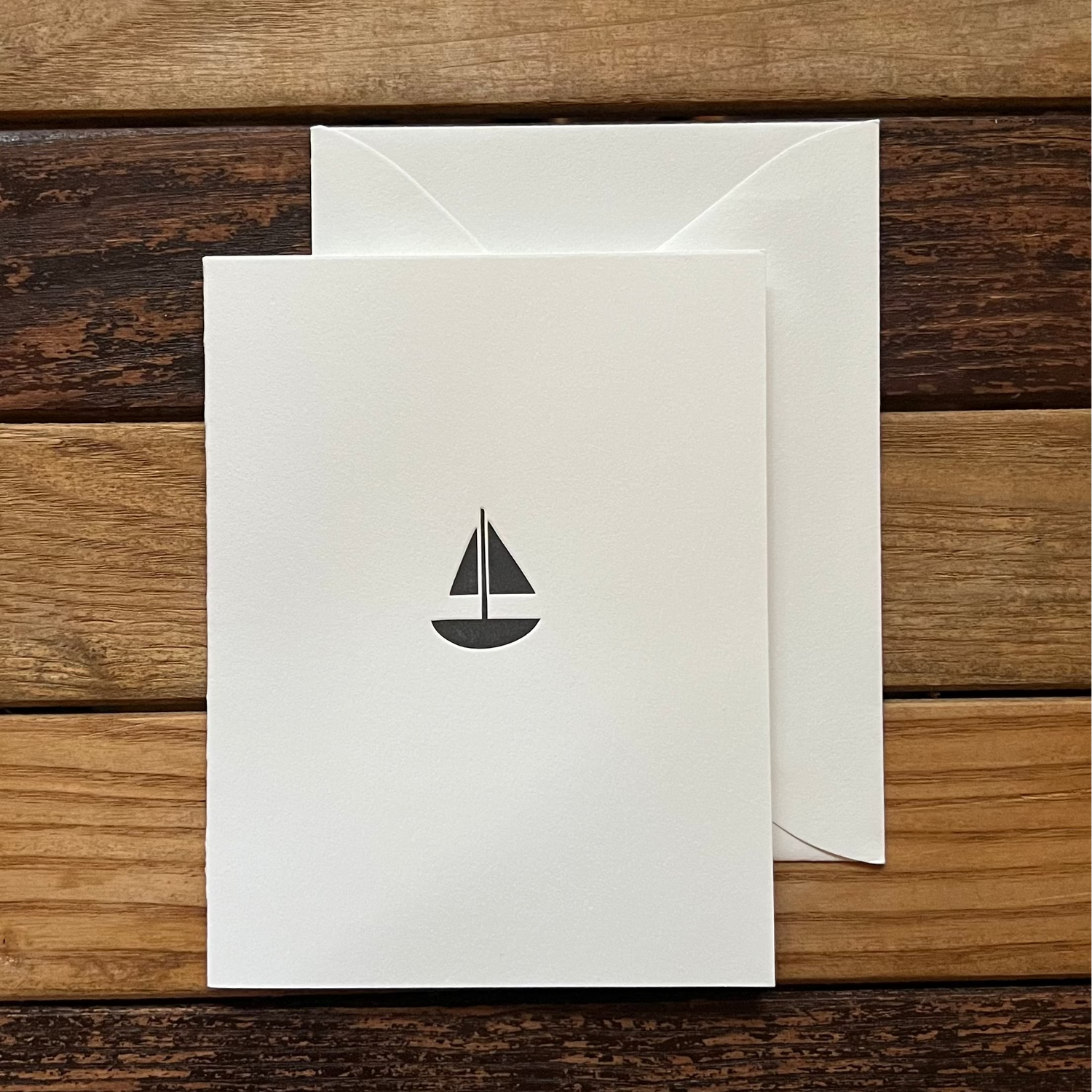 White card with a black sailboat design on a wooden surface