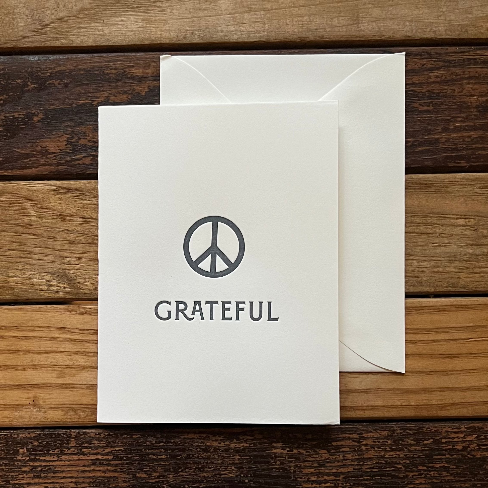 White card with peace symbol and 'GRATEFUL' text on a wooden surface