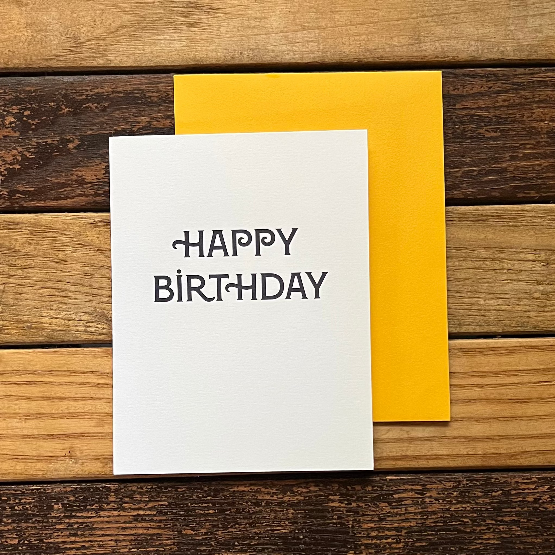 White card with 'Happy Birthday' text on a wooden surface