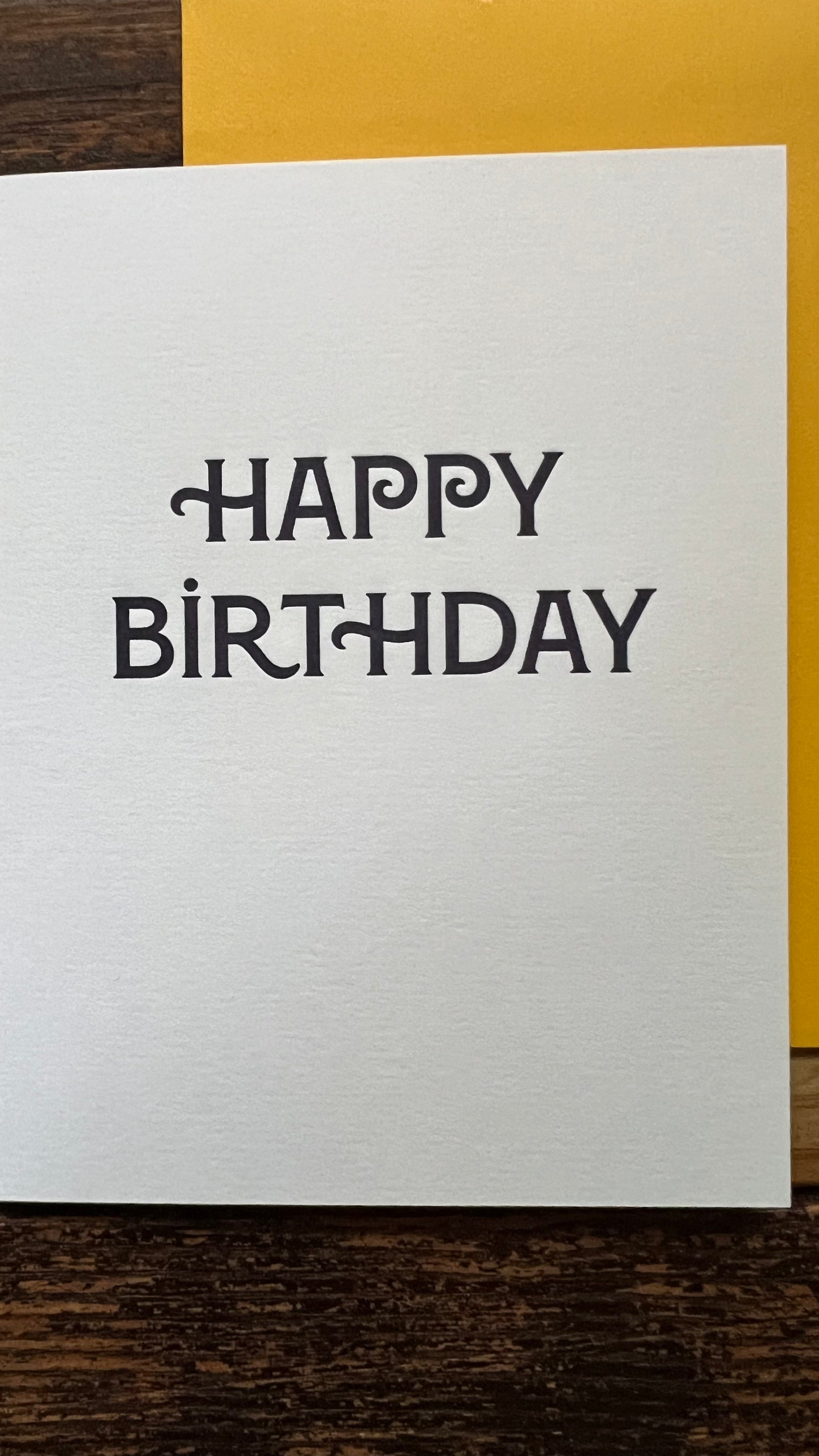 White card with 'Happy Birthday' text on a wooden surface