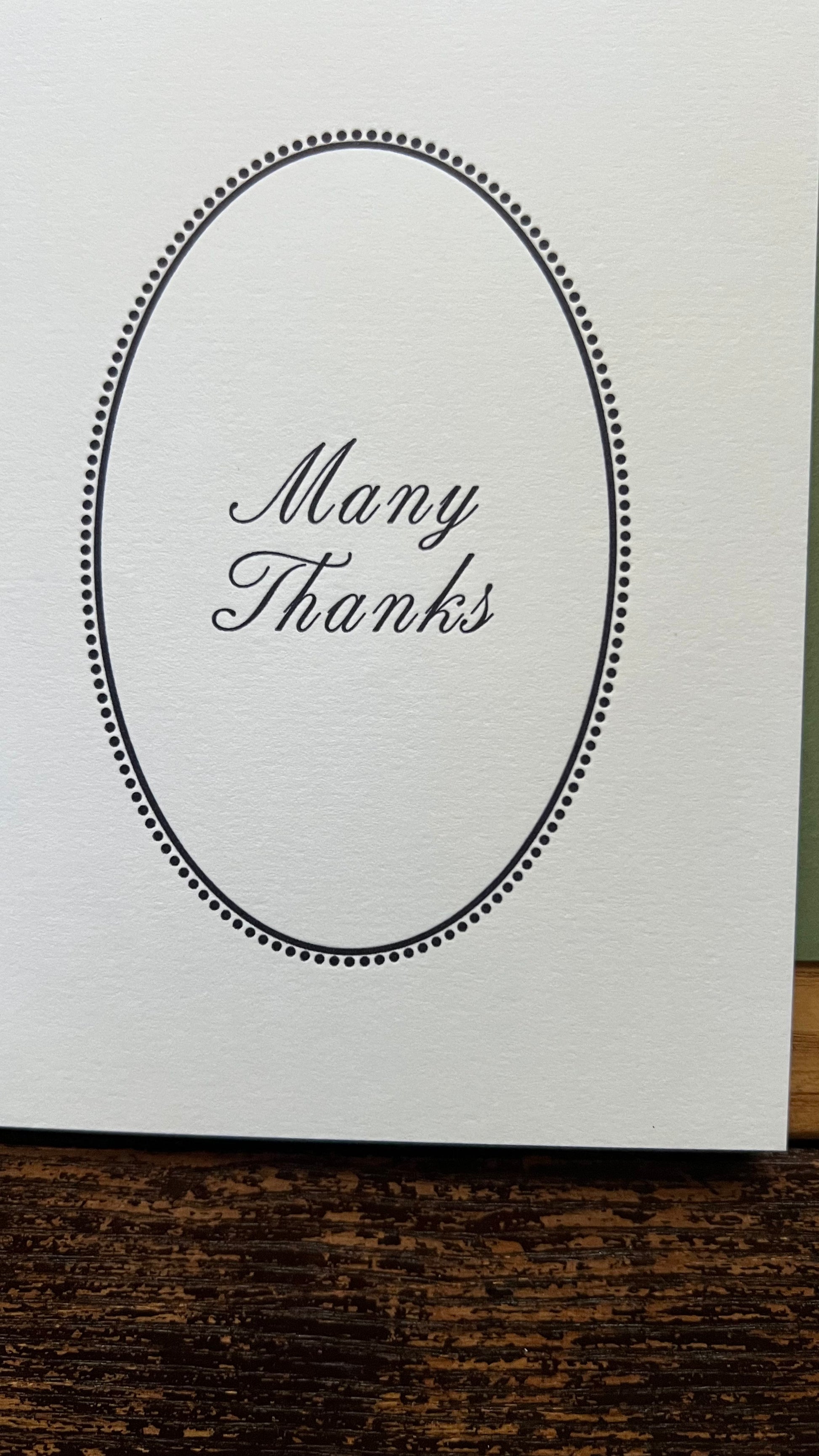 White card with 'Many Thanks' text in an oval frame on a wooden surface