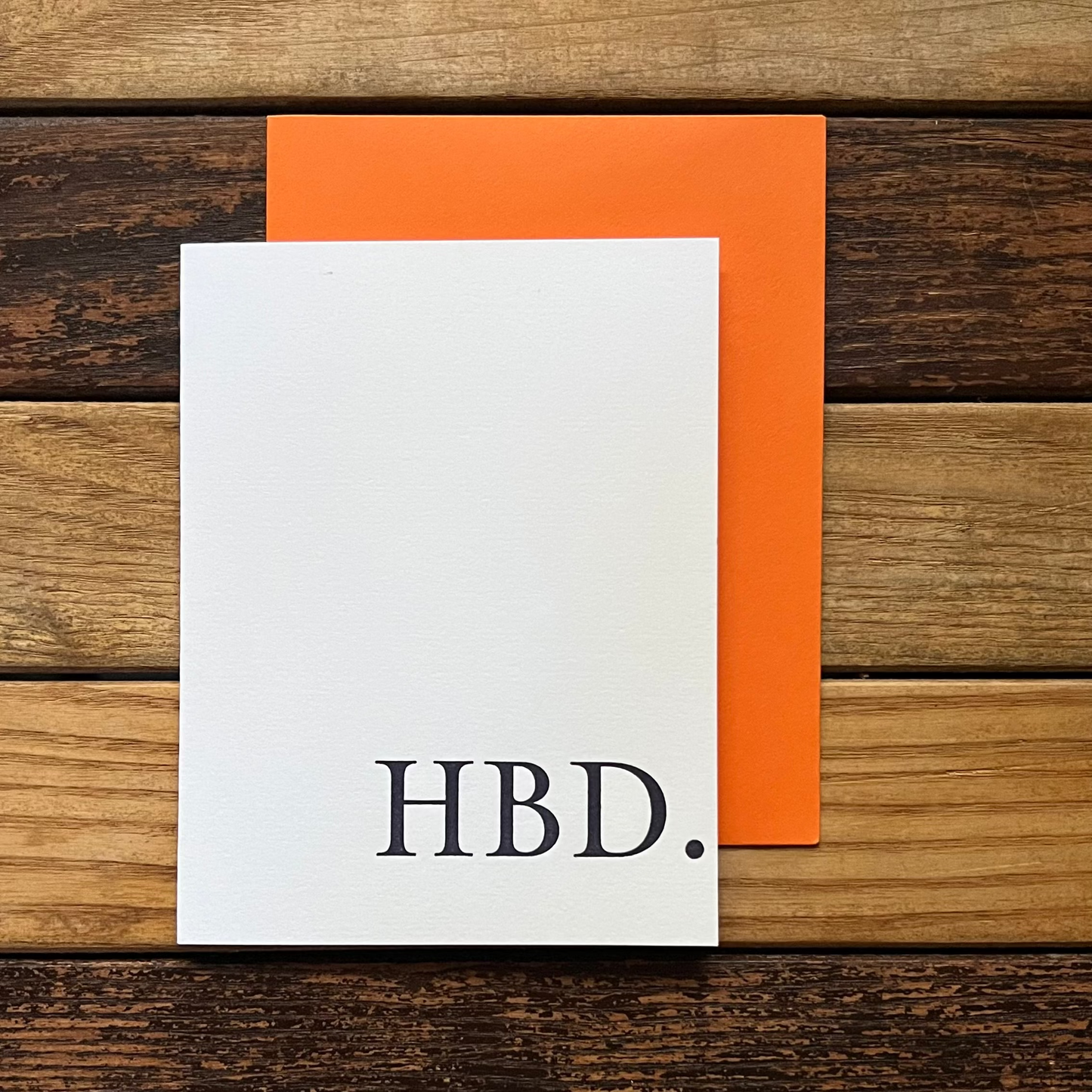 White card with 'HBD.' on an orange envelope against a wooden background