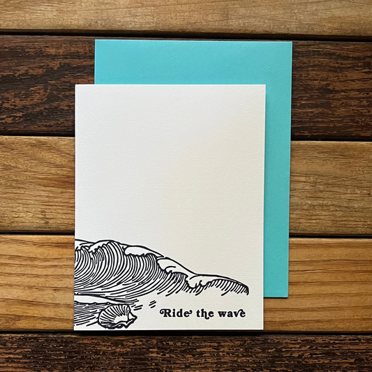 Greeting card with whale illustration and 'Ride the wave' text on a wooden surface