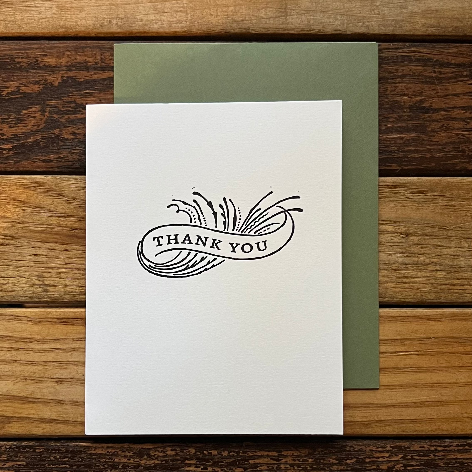 White card with 'Thank You' design on a wooden surface
