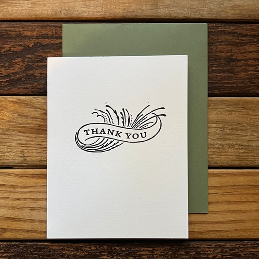 White card with 'Thank You' design on a wooden surface
