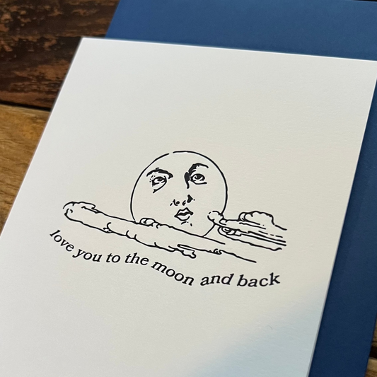 Greeting card with moon and text 'love you to the moon and back' on a wooden surface